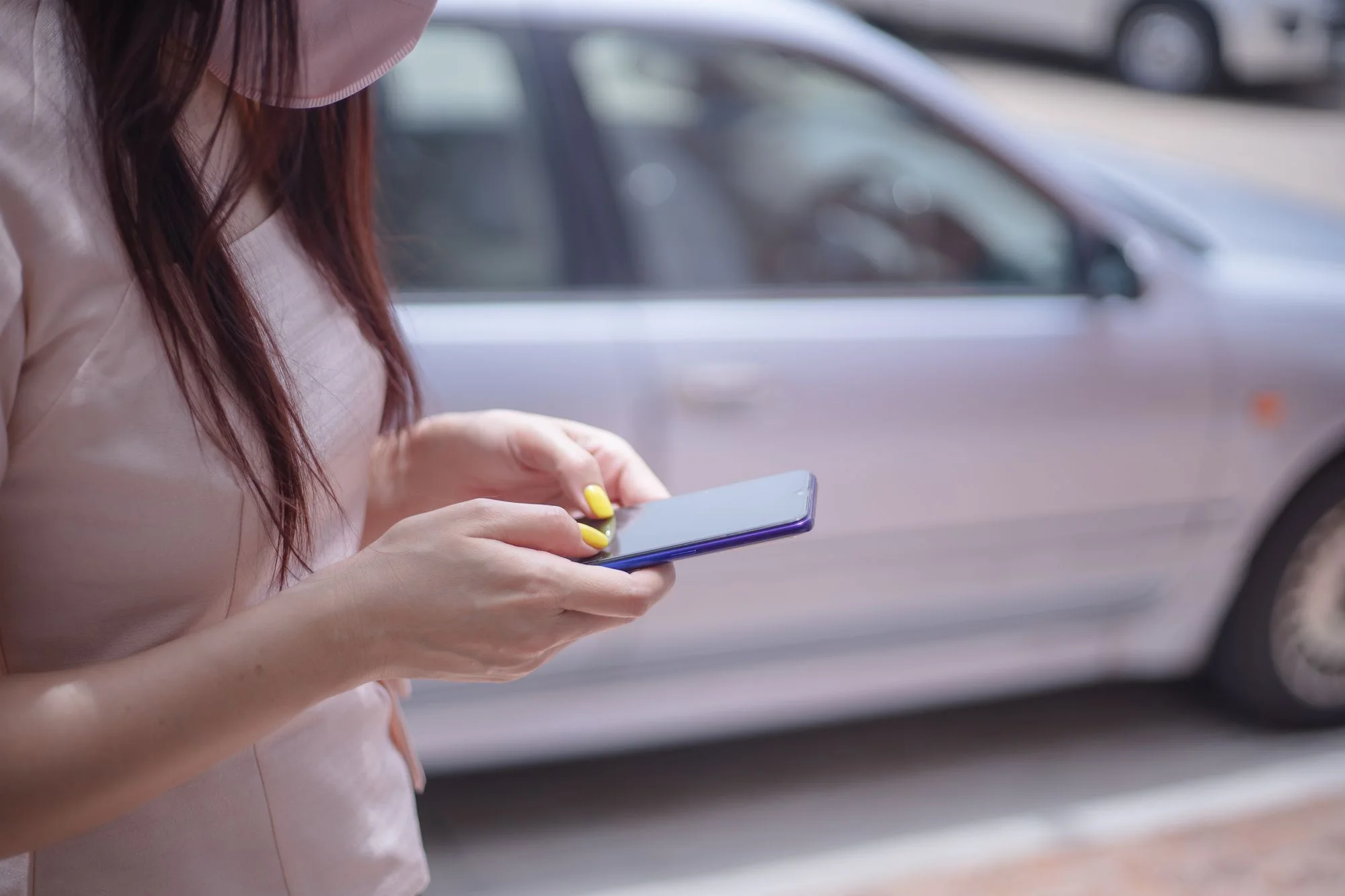Vrouw typt op haar telefoon naast haar auto