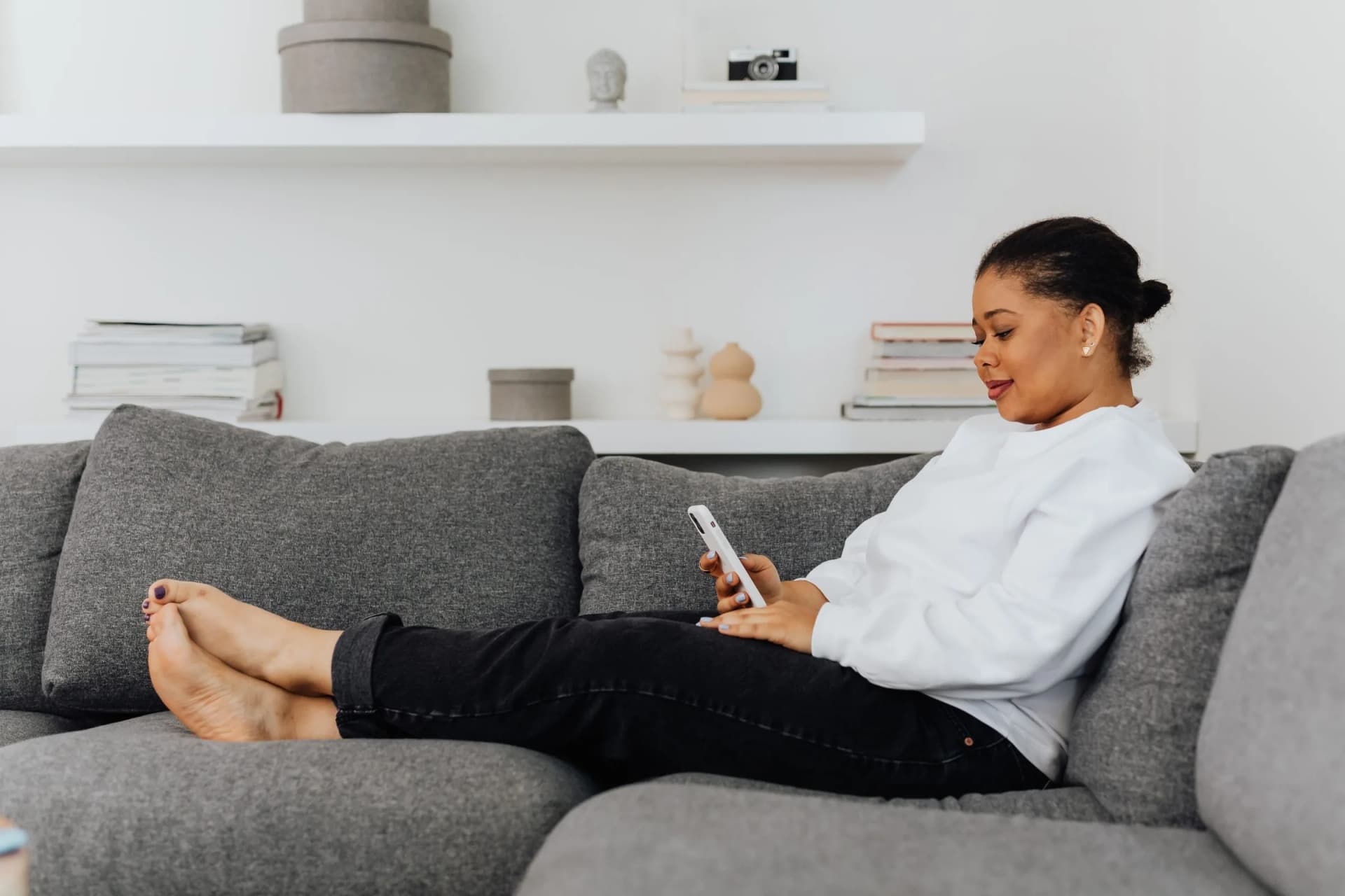 Jonge vrouw op een grijze bank kijkt op haar telefoon